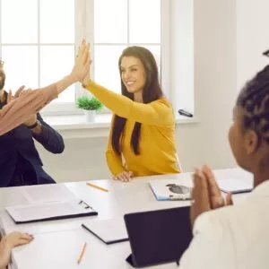 Happy women high five each other as they celebrate success during meeting with their business team