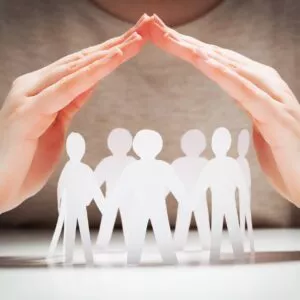 Paper people under hands in gesture of protection.. concept of insurance